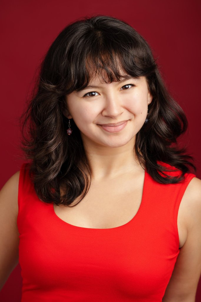 Nova Gomez, dressed in bright red, smiles at the camera/